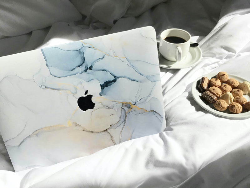 coque macbook en marbre bleu célestine sur des draps blancs avec un café et des gâteaux